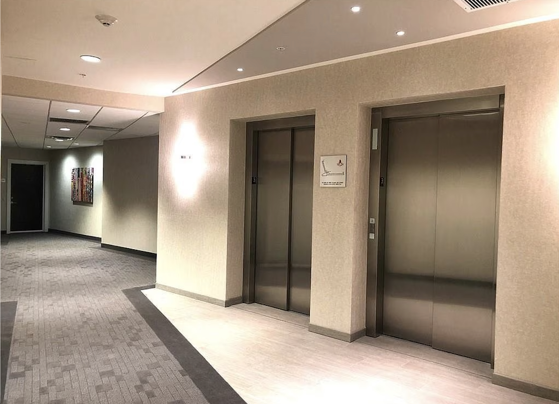 Upper-floor elevator landing with artwork and patterned carpeting