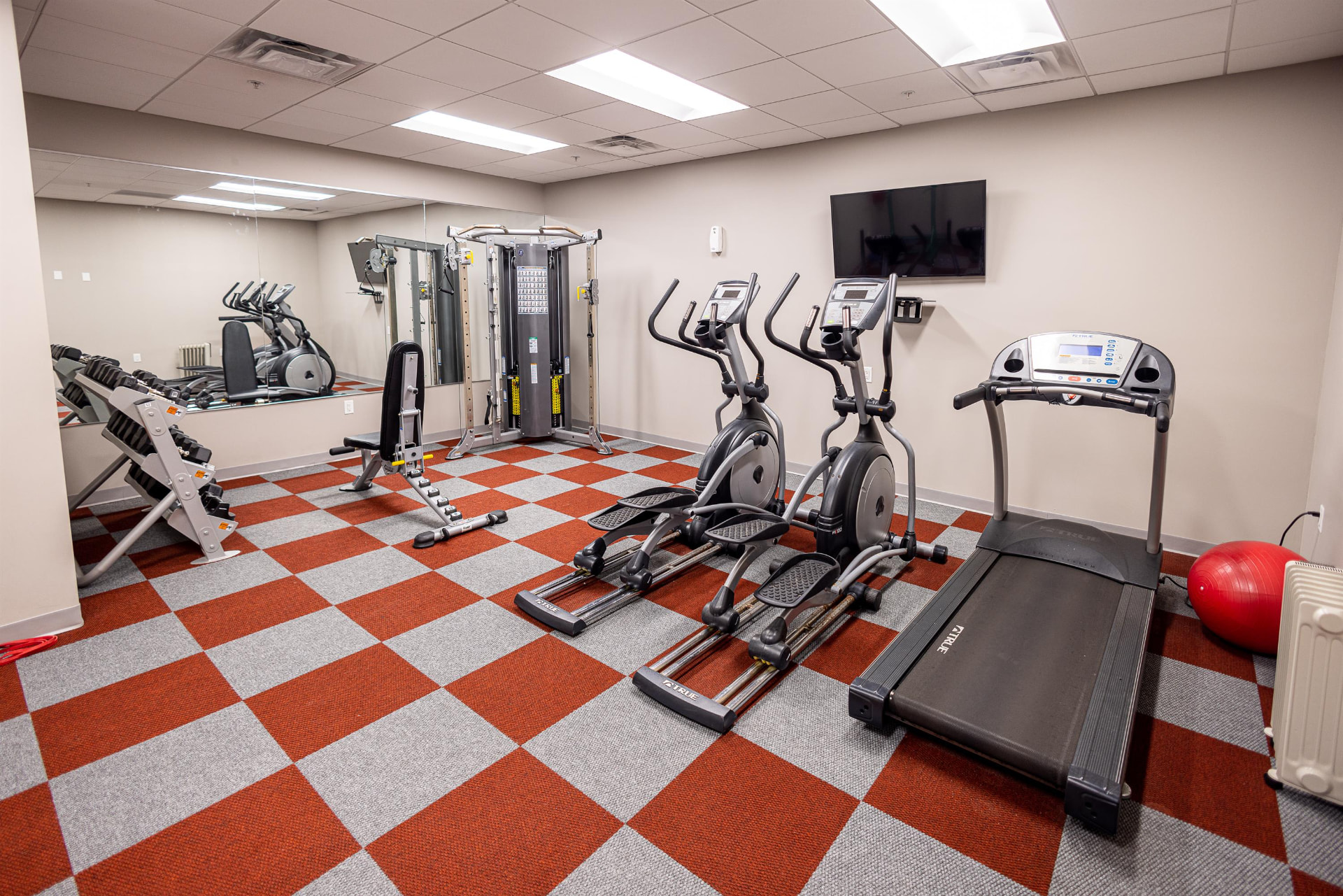 Resident fitness center with cardio machines, weights and a mirrored wall